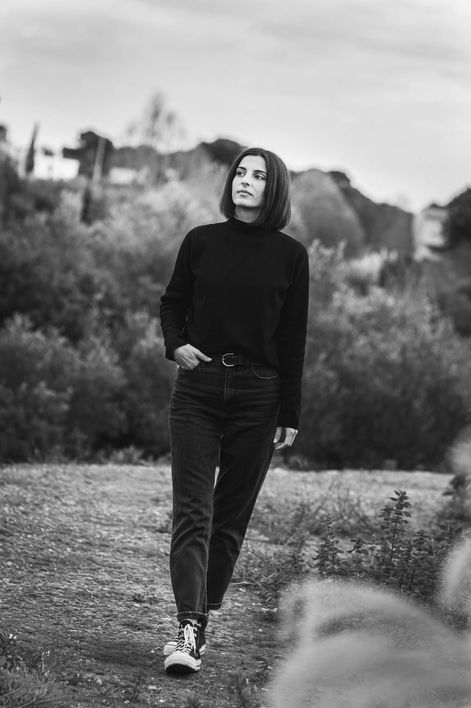 Portrait en pied en noir et blanc d'une femme marchant en tenue sombre décontractée dans un paysage naturel à La Ciotat.