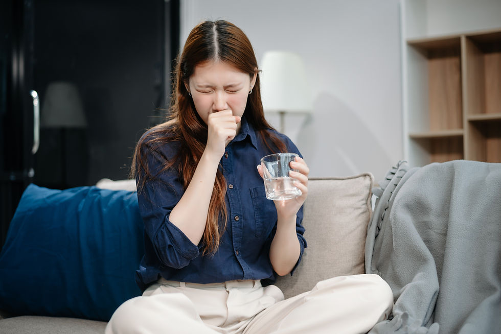 Young woman sitting on a couch holding a glass of water while covering her mouth as if nauseous. Image illustrates common GLP-1 medication side effects like nausea and dry mouth that may contribute to dental issues such as “Ozempic teeth.”