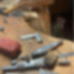 Auf diesem Bild sieht man die Werkzeuge eines Goldschmiedes. Einen Hammer, Winkelmesser, ein Stahllineal, Polierpaste, einen Fingerschutz und Silberreste.