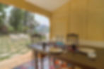 Dining area with the dining table and crockery with a view of trees and the garden.