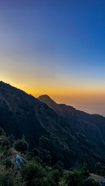A view of the Himalayan range with sun setting and hills covered with foliage.
