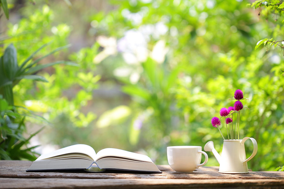 Open book, teacup, and purple flowers on a wooden table outdoors