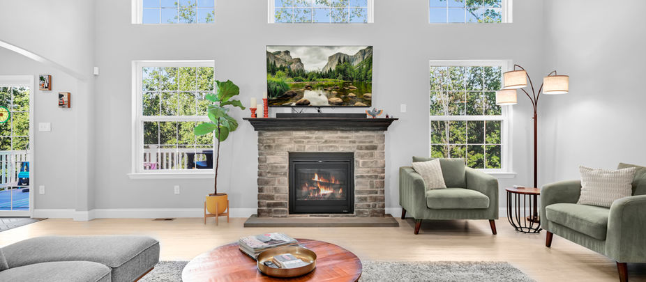 Bright living room with fireplace, large windows, neutral finishes and green accent chairs.