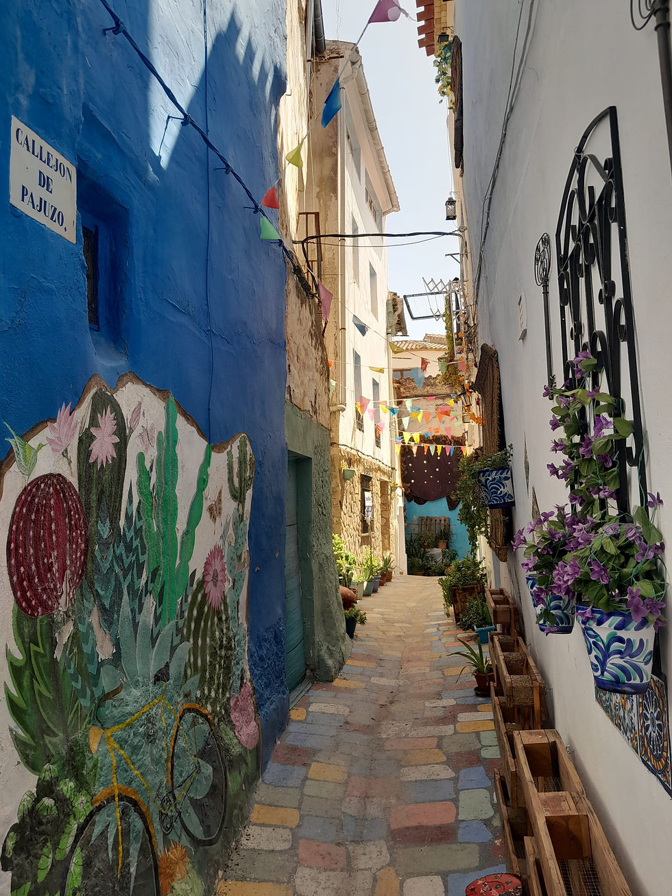 Ruelle étroite du Callejón de Pajuzo à Chelva avec fresque de cactus, pavés colorés et guirlandes de fanions
