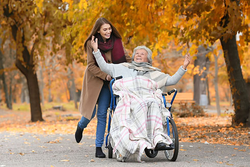 A happy young woman pushes an elderly woman in a wheelchair through a park in autumn_