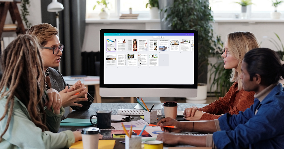 Four people sit around a table discussing in front of a large monitor displaying a website. The room has plants and a bright atmosphere.