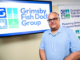 The new chief executive standing in front of a monitor and banner with the new branding for Grimsby Fish Dock Group displayed.