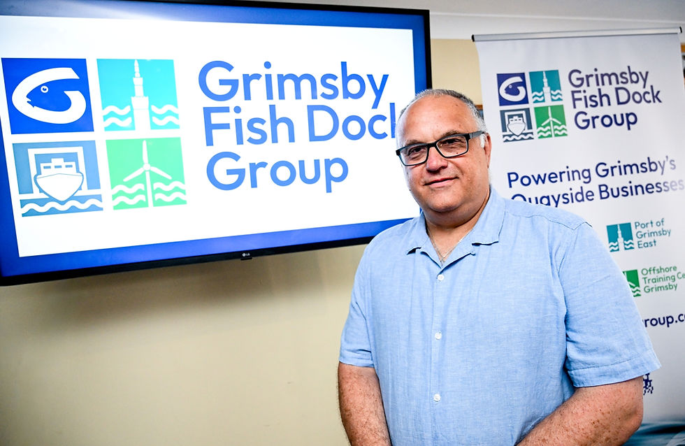 The new chief executive standing in front of a monitor and banner with the new branding for Grimsby Fish Dock Group displayed.