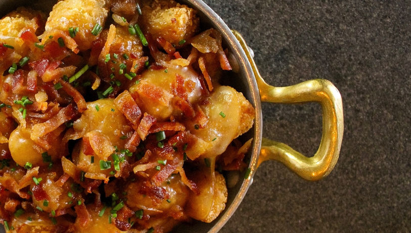 closeup overhead view of a serving dish filled with chunks of meat and garnished with assorted chopped herbs & vegetables in a nice-looking sauce, one gold handle is visible over a hard surface