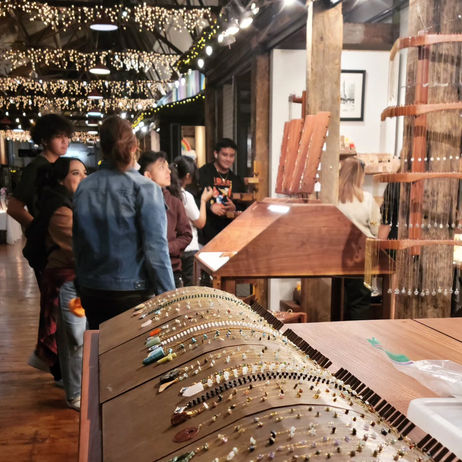 gemstone necklaces in foreground on a curving display mount, then people shopping the wares in middle space looking at other displays, and the atrium of CPH stretching into the distance, festooned with white teas lights, probably Christmas season?
