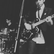 Band playing guitar and drums at a venue, black and white image.