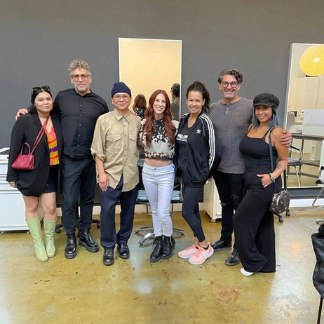 Nathan Nguyen standing with a group of seven people of mixed genders & races standing in an open space in the iLO Collective Salon & Apothecary, arm in arm, probably a post-class remebrance shot, gray wall in back, polished concrete flooring