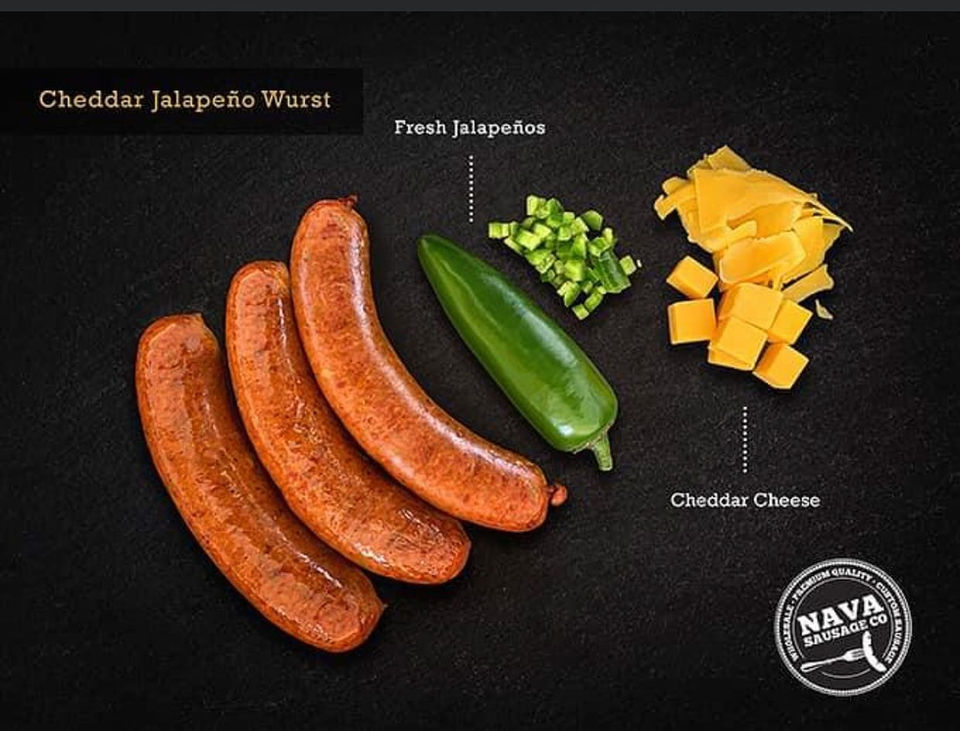 Magazine-ad style photo looking straight down on a very dark surface with 3 uncooked sausages, side by side, 1 large jalapeño pepper, chunks of cheddar cheese in little labeled groups as if to say, “Here’s the simple ingredients.” (Cheddar Jalapeño Wurst sausages!)