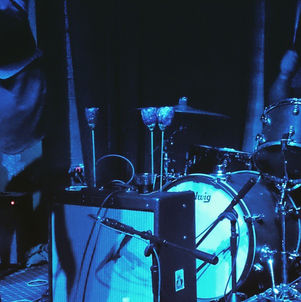Drum set on stage with microphones, blue lighting, and Flyway Bar+Nightclub