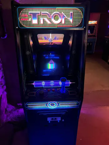 TRON arcade game cabinet, glowing blue, in a dim arcade.