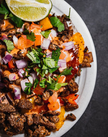 Overhead straight-down look at about half a plate of cubed beef and vegetables, spiced up with cilantro and a wedge of lime, on a corningware plate, sitting on a dark granite surface. Very fresh looking.