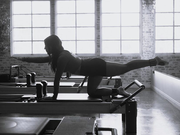Woman in bird-dog pose on a Pilates reformer, arm and leg extended.