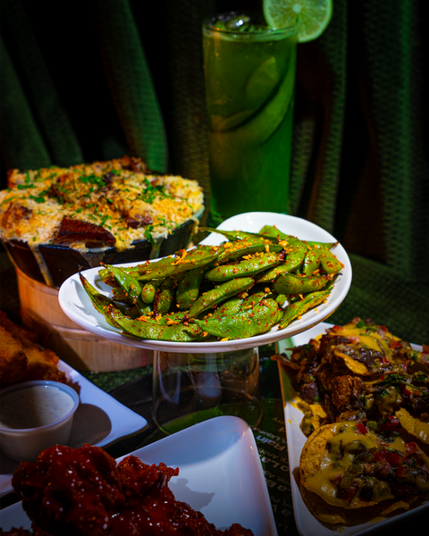 Various foods, including edamame, and a green cocktail, on a table. V Lounge