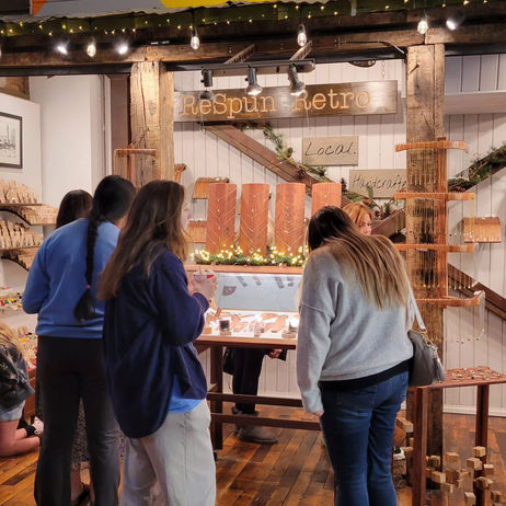 four women stopping to look at the wares displayed on & in various tasteful wooden structures, the routered ReSpun Retro placard visible above on the back wall