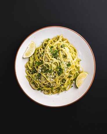 direct overhead view of a round ceramic plate of spaghetti noodles and pesto with basil garnish and wedges of lime