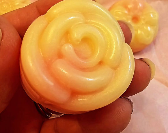 woman's fingers & thumb holding up a slightly larger thick rose-petal motifed yellow soap, one other visible underneath in background on cloth