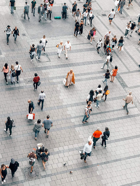 an overhead view of a busy wide-open plaza surface of large square pavers tightly packed, various small groups of different types of people walking