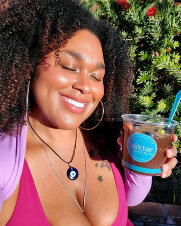 Smiling woman enjoys NÉKTER JUICE BAR drink out in the bright sunshine with her eyes closed in pleasure, holding up her cup