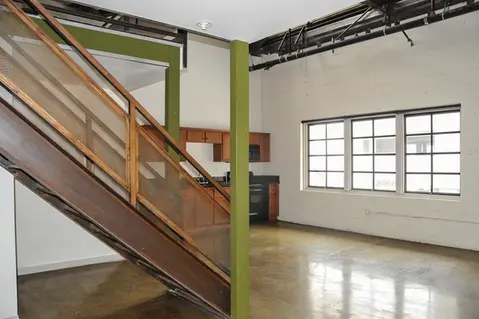 an interior, lower-level view of a work/live loft in the Packing House in Claremont, CA with shiny refinished concrete floor, large factory windows, white walls, a very sturdy metal staircase with wooden railings & painted green buttresses