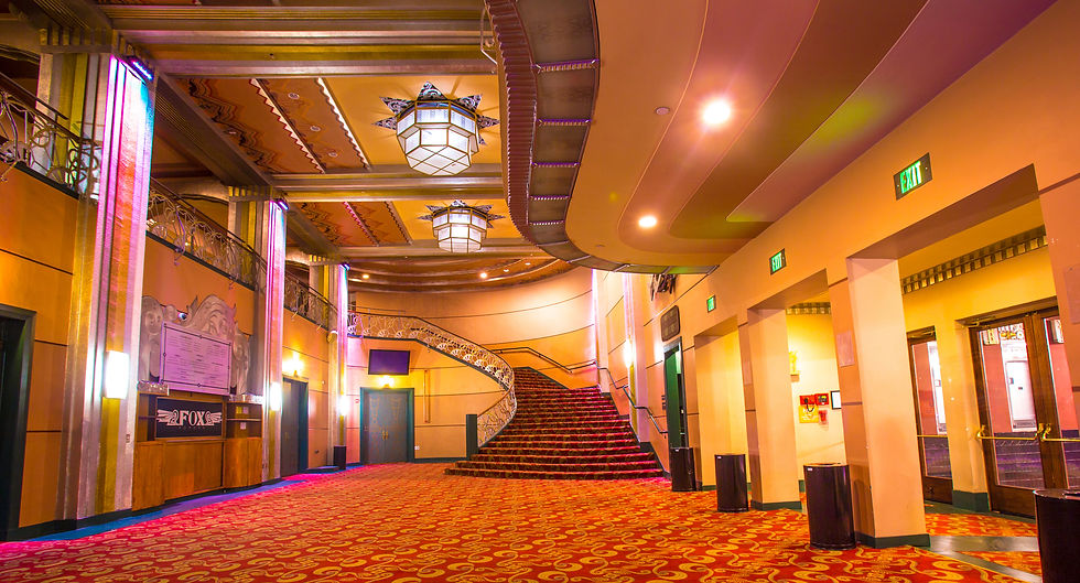gorgeous interior lobby of the Fox Theater in Pomona,featuring deep golds & reds, art deco styling & lighting, and a majestic sweeping staircase up to the mezzanine