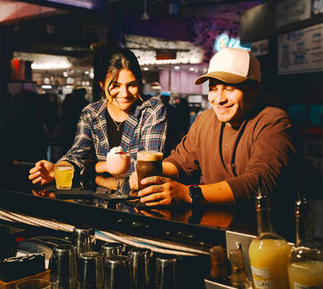A couple sits enjoying each other, conversation, and cocktails at Brass Monkey Social, all dark around their lit up faces.