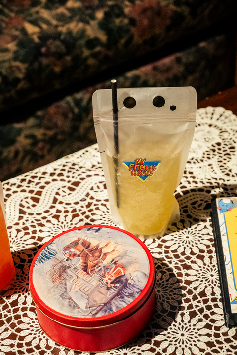 an yellow iced-drink baggy cocktail with straw poked into it nexted to a fingerbowl of snack on a doilied tablecloth