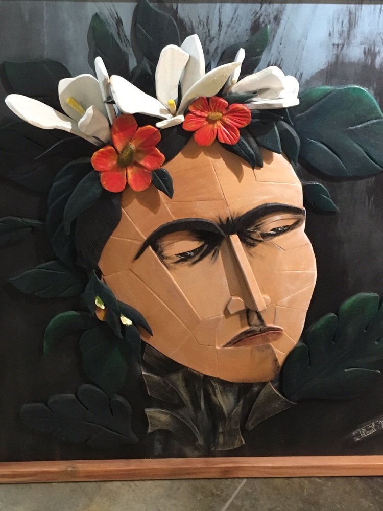 a closeup of a woman's face from a painted collage resembling Frida Kahlo with flowers in her hair and serious, somber look, surrounded by dark greens