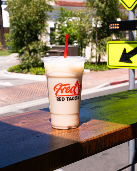 Fred Red Tacos drink with a straw, on a wooden table, outdoors.