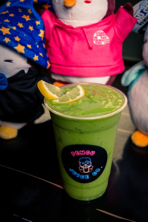 Green juice with lemon slice, Vibes up, and adorable penguin toys in background.