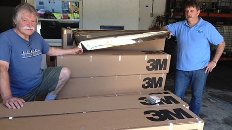 Two men smiling beside a pile of 3M boxes