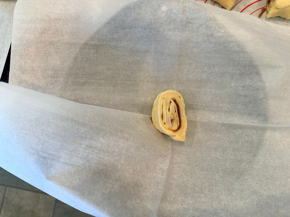 One piece of apple and cinnamon honey roll placed onto parchment paper in a baking pan.