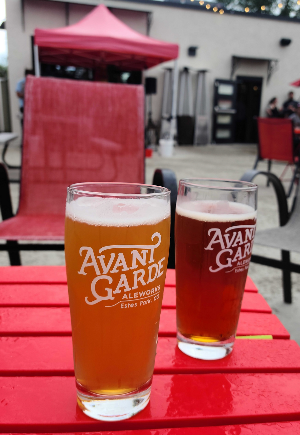 Two glasses of draft beer sitting on a red picnic table.