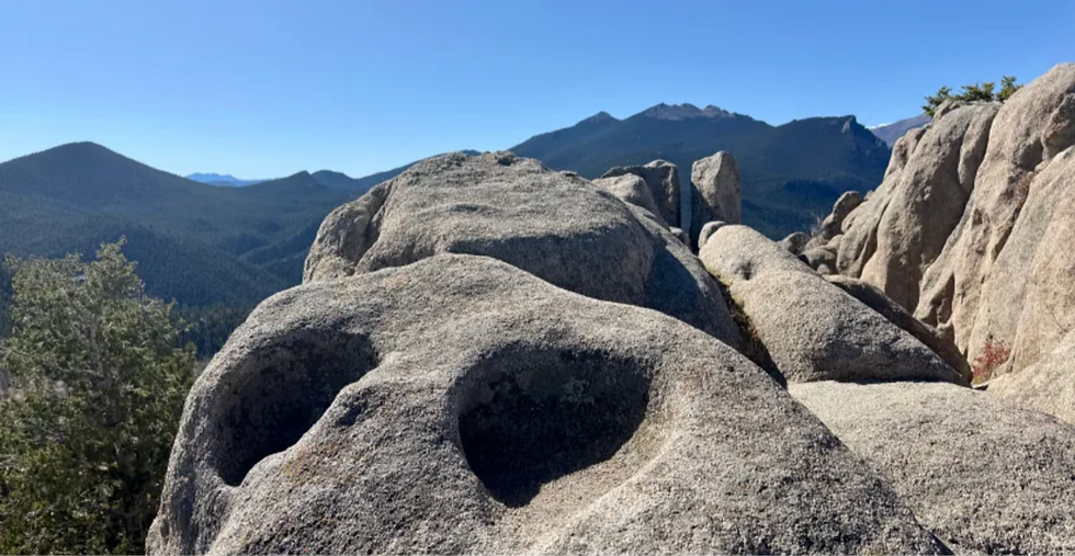 Granite boulders with weathered hollows overlook forested mountains under a clear blue sky.