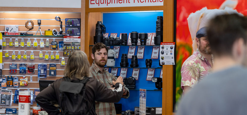 Equipment Rentals sign above cameras in a store, customers browsing selection.