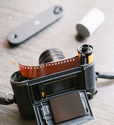 Open film camera with film roll and cartridge on wood surface, theshutterbug