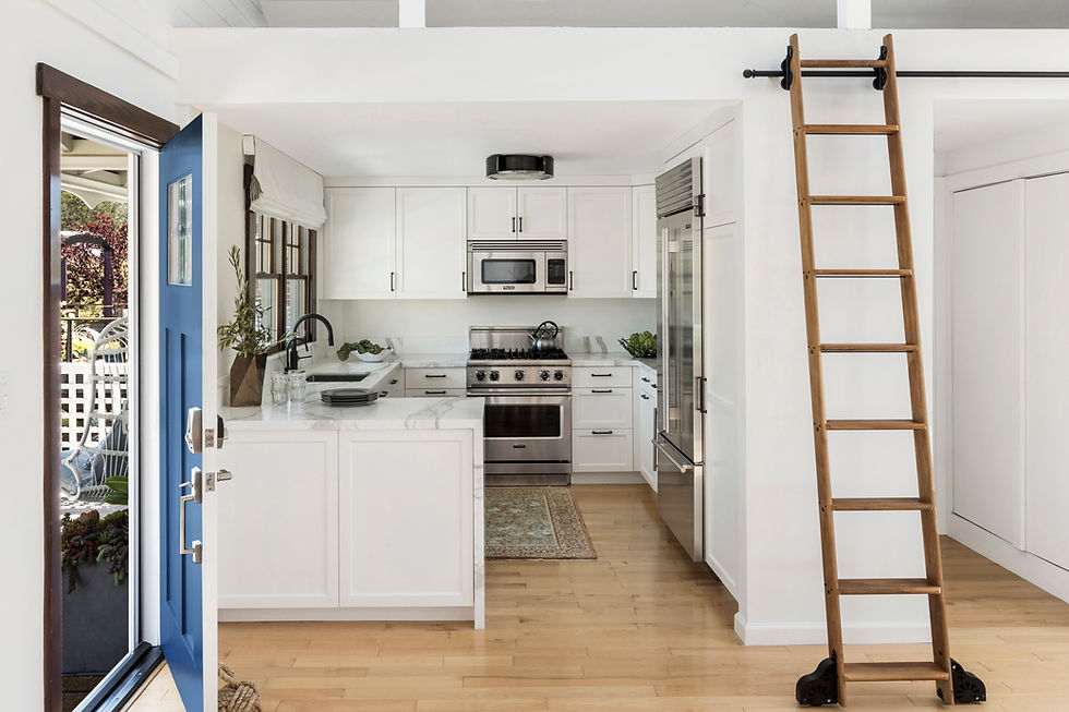 Bright white kitchen with stainless steel appliances, blue Dutch door, sliding library ladder, and warm wood floors in a custom Robin Heard Design home.
