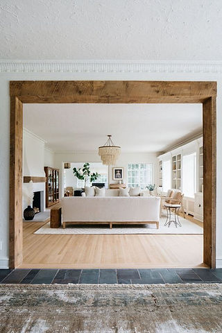 A spacious modern casually elegant living room framed by a rustic reclaimed wood archway, showcasing the blend of contemporary and rustic design elements using natural materials