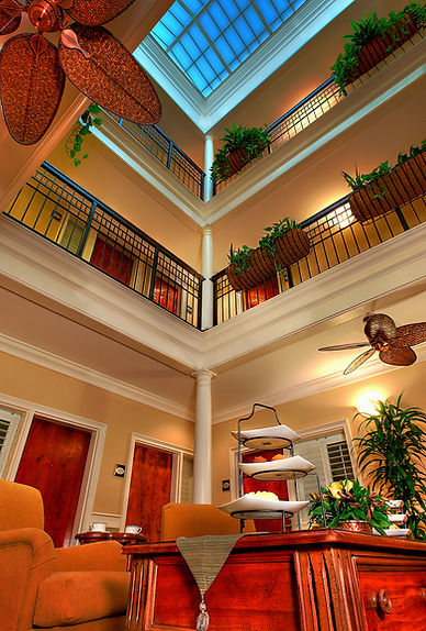 Multi-story interior atrium with skylight, wrought iron railings, hanging plants, and warm lighting showcasing upscale hospitality architecture.