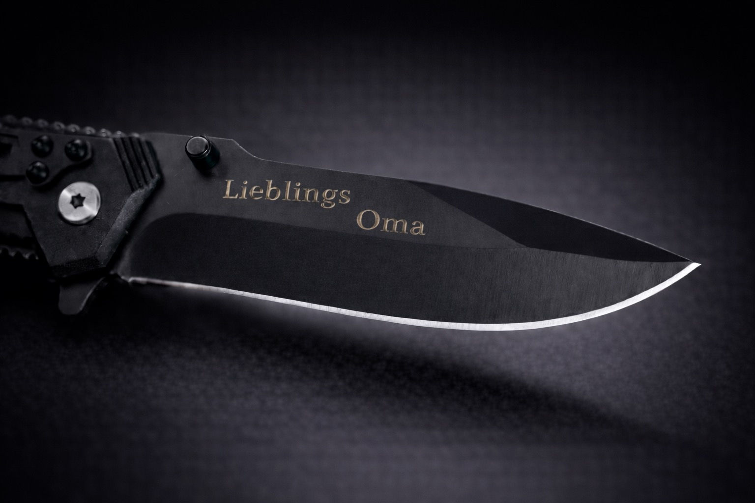 Schwarzes Klappmesser mit Gravur "LieblingsOma" auf der Klinge, edel inszeniert vor dunklem Hintergrund