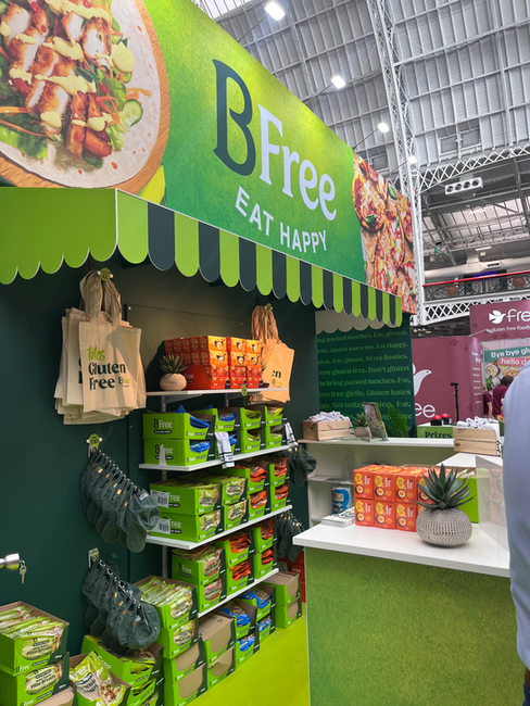 An exhibition stand for BFree Foods. Viewed from the side, the image shows a close up on the shop area, with lots of product and merch displayed under a market awning.