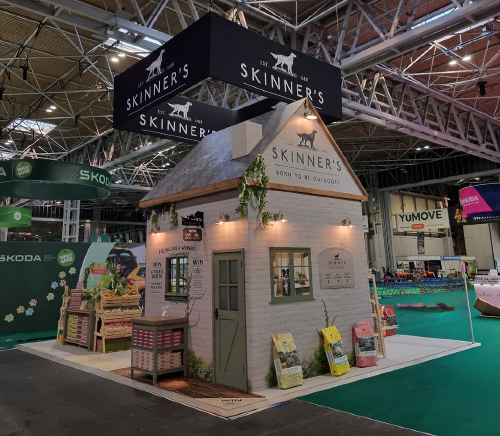 Skinner's stand at Crufts is shaped like a cottage, with their name and slogan ('born to be outdoors') written on the fascia. A competition is advertised around the window, and bags of dog food product settle around the edges. Four little lamps built into the walls light the olive green door and the exterior of the stand with a cosy yellow glow.