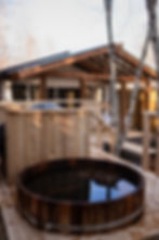 Wooden hot tub on a deck near a modern-rustic building, in a serene Luxury Glamping Franchise enviro
