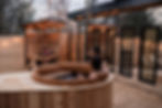 Relaxed couple in a wooden hot tub under string lights at Glamping, combining outdoor leisure with p