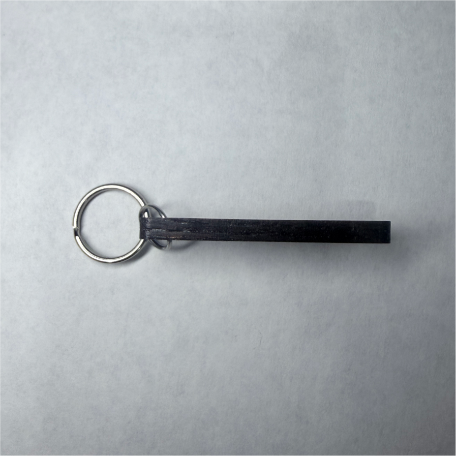 Thumbnail: Metal key ring with dark rectangular bar on a gray surface.