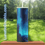 Thumbnail: Blue artistic tumbler with straw, LunaticGraphix.com, on wooden surface outdoors.